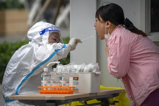 A worker wearing a protective suit swabs a woman's throat for a COVID-19 test at a coronavirus testing site in Beijing, Thursday, June 9, 2022. Thousands of COVID-19 testing booths have popped up on sidewalks across Beijing and other Chinese cities in the latest twist to the country's "zero-COVID" strategy. (AP Photo/Mark Schiefelbein)