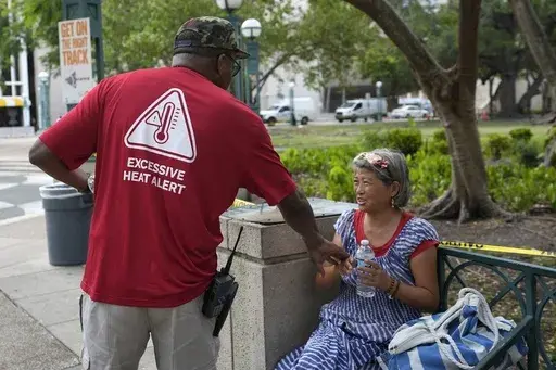 Ricky Leath, an outreach specialist with the City of Miami, talks with Bei Zhao, right, as he works with the Miami-Dade County Homeless Trust to distribute bottles of water and other supplies to the homeless population, helping them manage high temperatures, May 15, 2024, in Miami. (AP Photo/Lynne Sladky, File)