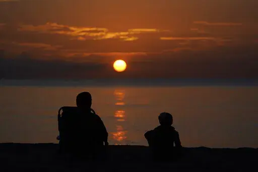 A pair of beach goers watch the sun rise over the Atlantic Ocean, Friday, June 10, 2022, in Surfside, Fla. All the experts predicted this would be a more active than normal hurricane season, but then nothing happened. Scientists think a persistent patch of dry air is the reason storms aren't forming. (AP Photo/Wilfredo Lee, File)