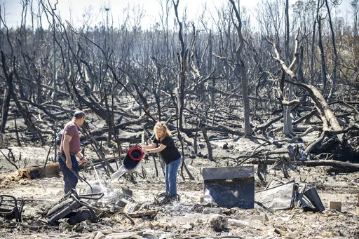Hector Rivera and Wandi Blanco put water on hotspots behind their home in Panama City, Fla., Saturday, March 5, 2022, following a wildfire that started Friday. The fire destroyed two homes next to them and melted the siding off of their home. (Mike Fender/News Herald via AP)