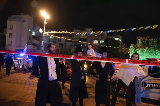 Ultra-Orthodox Jews stand behind police tape after a stabbing attack in the town of Elad, Israel, Thursday, May 5, 2022. Israeli medics say at least three people were killed in a stabbing attack near Tel Aviv on Thursday night. Israeli police said they suspect it was a militant attack. (AP Photo/Maya Alleruzzo)
