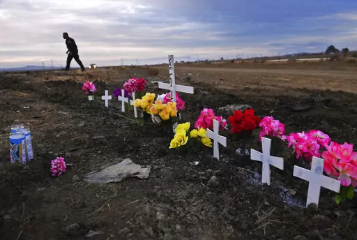 A row of crosses form a memorial along Highway 33 as police officers survey the scene a day after a crash killed nine people south of Coalinga, Calif., Saturday, Jan. 2, 2021. Investigators said the driver of an SUV involved in the crash was drunk and didn't have a license. The National Transportation Safety Board will use a final report on the crash to launch an effort to lobby for regulations requiring alcohol breath testing devices on all new vehicles. (Eric Paul Zamora/The Fresno Bee via AP)