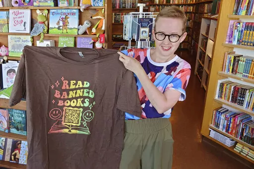 Former Norman High School English teacher Summer Boismier holds up a T-shirt with a QR code link to the Brooklyn Public Library at the Green Feather Book Company in Norman, Okla., on Oct. 6, 2022. Boismier found herself at the center of a political firestorm in Oklahoma after providing the QR code to her students and ultimately left her teaching job. (AP Photo/Sean Murphy)