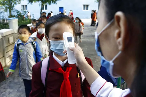 A teacher takes the body temperature of a schoolgirl to help curb the spread of the coronavirus before entering Kim Song Ju Primary School in Central District in Pyongyang, North Korea, on Oct. 13, 2021. According to North Korea, its fight against COVID-19 has been impressive: About 3.3 million people have been reported sick with fevers, but only 69 have died.   (AP Photo/Cha Song Ho, File)