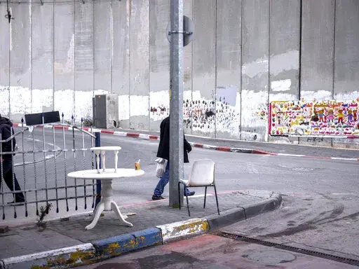 Palestinians walk by a section of the Israeli separation barrier in the West Bank village of Abu Dis in the outskirts of Jerusalem, Monday, Jan. 31, 2022. Twenty years after Israel decided to built its controversial separation barrier amid a wave of Palestinian attacks, it remains in place, even as Israel encourages its own citizens to settle on both sides and admits tens of thousands of Palestinian laborers. (AP Photo/Oded Balilty)
