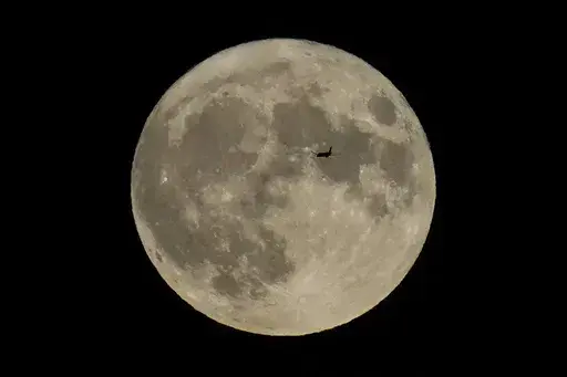 A plane passes in front of the moon, Aug. 30, 2023, in Chicago. Scientists have confirmed a cave on the moon, not far from where Neil Armstrong and Buzz Aldrin landed 55 years ago this week, and suspect there are hundreds more that could house future astronauts. (AP Photo/Kiichiro Sato, file)