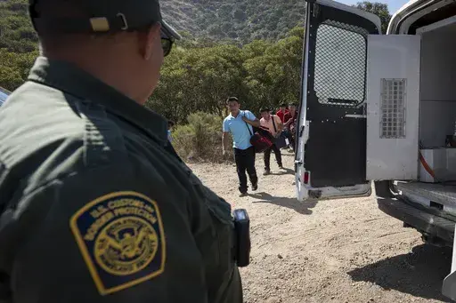 A Border Patrol agent leads a group of migrants seeking asylum towards a van to be transported and processed, Wednesday, June 5, 2024, near Dulzura, Calif. President Joe Biden on Tuesday unveiled plans to enact immediate significant restrictions on migrants seeking asylum at the U.S.-Mexico border as the White House tries to neutralize immigration as a political liability ahead of the November elections. (AP Photo/Gregory Bull)