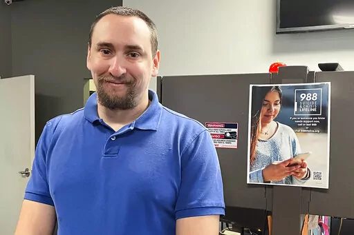 988 Call Center Director Jamieson Brill poses for a photo in front of a desk where work workers take calls around the clock at a facility in Hyattsville, Md., Oct. 7, 2022. Brill works in one of more than 200 call centers fanned out around the country tasked with answering an uptick in calls around the clock from people considering suicide or experiencing a mental health emergency. (AP Photo/Amanda Seitz)