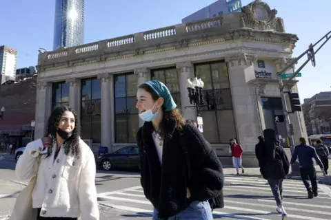 Passers-by wear masks under their chins as they chat with one another while crossing a street, in Boston, Wednesday, Feb. 9, 2022. Students and staff at public schools in Massachusetts will no longer be required to wear face coverings while indoors starting Feb. 28, state officials said Wednesday, Feb. 9, 2022. (AP Photo/Steven Senne, File)