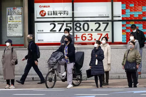 People wait for a traffic light to change in front of an electronic stock board showing Japan's Nikkei 225 index at a securities firm Thursday, March 2, 2023, in Tokyo. Asian stock markets were mixed Thursday after signs of enduring upward pressure on American prices added to expectations of higher interest rates for longer. (AP Photo/Eugene Hoshiko)