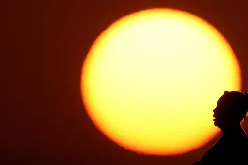 A woman is silhouetted against the setting sun as triple-digit heat indexes continue in the Midwest, Aug. 20, 2023, in Kansas City, Mo. The rate Earth is warming hit an all-time high in 2023 with 92% of last year’s surprising record-shattering heat caused by humans, top scientists calculated. (AP Photo/Charlie Riedel, File)