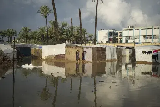 Two Palestinian girls attempt to walk through a flooded area after a night of heavy rainfall at a tent camp for displaced Palestinians in Deir al-Balah, central Gaza Strip, Thursday Jan. 23, 2025. (AP Photo/Abdel Kareem Hana)