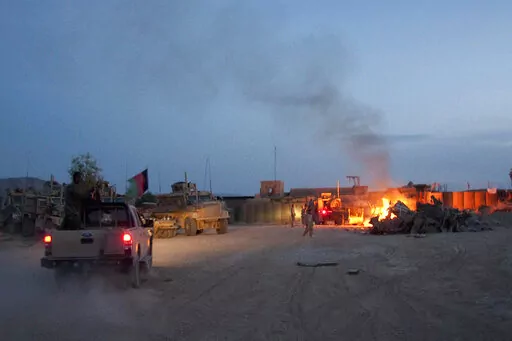 In this April 28, 2011, photo, an Afghan National Army pickup truck passes parked U.S. armored military vehicles, as smoke rises from a fire in a trash burn pit at Forward Operating Base Caferetta Nawzad, Helmand province south of Kabul, Afghanistan. The House is poised to pass legislation that would dramatically boost health care services and disability benefits for veterans exposed to burn pits in Iraq and Afghanistan. (AP Photo/Simon Klingert, File)