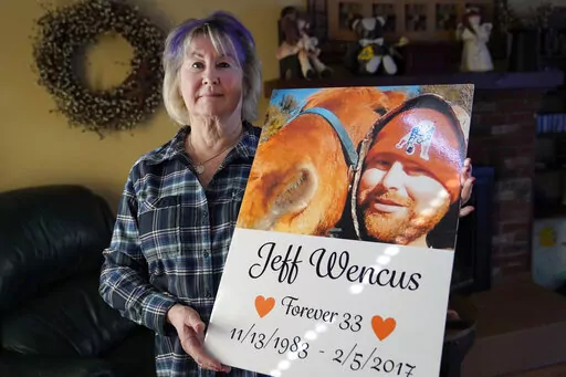 Lynn Wencus, of Wrentham, Mass., holds a poster, with a likeness of her son Jeff, at her home, in Wrentham, Wednesday, March 2, 2022. Wencus lost her son to a heroin overdose in 2017. OxyContin maker Purdue Pharma and virtually all U.S. states have agreed to a new settlement of opioid lawsuits. The deal reached Thursday, March 3, 2022, would require members of the Sackler family who own the drugmaker to pay $5.5 billion to $6 billion in cash. They also apologized. A bankruptcy judge must still a