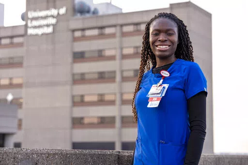 In this Feb. 1, 2022, photo provided by University of Louisville Hospital, Faith Akinmade, an ICU nurse at the University of Louisville Hospital in Louisville, Ky., who is originally from Nigeria, poses for a photo in front of the hospital. After completing college in the United States, Akinmade has been working at the hospital, but her work permit is set to expire in March and she said she needs it renewed, or her green card approved, to stay on the job. Hospitals and recruiters are hoping inte