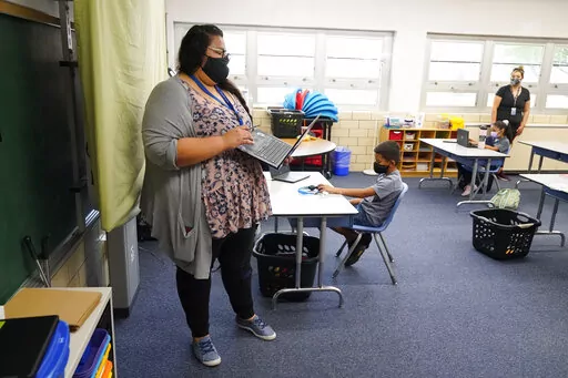 Teacher Jessica Flores directs students as they work on laptops in a classroom in Newlon Elementary School on, Aug. 25, 2020, in Denver, Colo., which is one of 55 Discovery Link sites set up by Denver Public Schools where students are participating in remote learning during the COVID-19 pandemic. Colorado lawmakers are considering joining eight other states in an agreement that would eliminate many of the requirements for teachers to get licensed when they move within the member states. (AP Phot