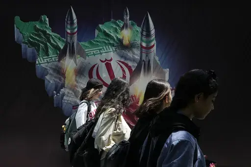 Iranian women without a mandatory headscarf, or hijab, walk past a banner showing missiles being launched from Iranian map in northern Tehran, Iran, April 19, 2024. (AP Photo/Vahid Salemi, File)