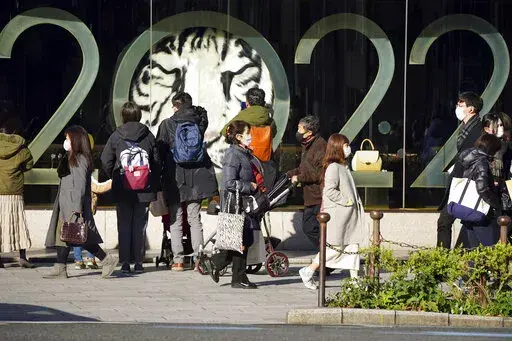 People wearing protective masks to help curb the spread of the coronavirus stand outside a window displaying a 2022 New Year celebration along a street Wednesday, Dec. 29, 2021, in Tokyo. (AP Photo/Eugene Hoshiko)