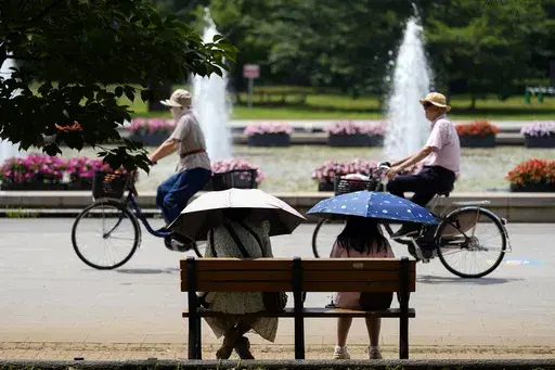 People holding parasols sit on the bench under an intense sun at a park in Tokyo, July 8, 2024. Japan’s total population marked the 15th straight year of decline, according to government data released Wednesday, July 24. (AP Photo/Eugene Hoshiko, File)
