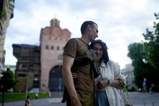 Stand-up comics Serhiy Lipko and Anastasia Zukhvala embrace during an interview with The Associated Press on their wedding day in Kyiv, Ukraine, Saturday, June 11, 2022. Lipko and Zukhvala are among those using humor as a weapon, and to keep spirits up. But he'll soon have a real weapon in his hands, because he's going into battle. (AP Photo/Natacha Pisarenko)