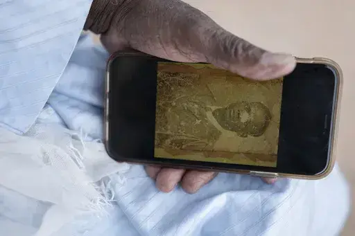 Biram Senghor, whose father was killed in 1944, holds a phone with a photo of his father, in Rufisque, Senegal, Thursday, Nov. 28, 2024. (AP Photo/Sylvain Cherkaoui)