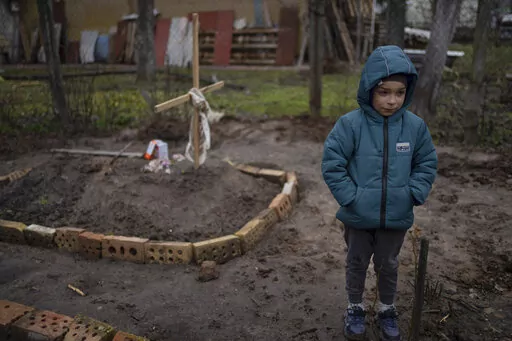 In the courtyard of their house, Vlad, 6, stands near the grave of his mother, who died, on the outskirts of Kyiv, Ukraine, Monday, April 4, 2022. Vlad's mother died last month when the family was forced to shelter in a basement during the occupation by the Russian army. The family still doesn't know what illness caused her death. (AP Photo/Rodrigo Abd)