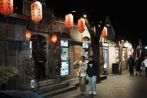 Shoppers walk at a tourist attraction area, Nanluogu Alley in the evening in downtown Beijing, China, Saturday, March 8, 2025. (AP Photo/Vincent Thian)
