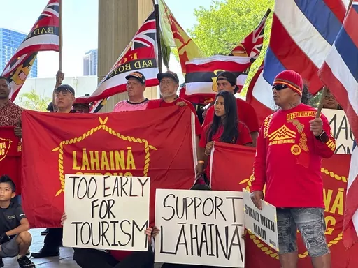 Lahaina residents and their supporters hold signs and flags at the Hawaii State Capitol in Honolulu on Tuesday, Oct. 3, 2023, at a news conference about a petition asking Hawaii Gov. Josh Green to delay plans to reopen a portion of West Maui to tourism starting this weekend. The petition signed by more than 14,000 people comes amid a fierce and anguished debate over when travelers should return to the region, home to the historic town of Lahaina that was destroyed in the deadliest U.S. wildfire 