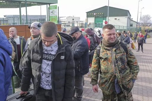 Polish volunteer Jedrzej, 34, in military uniform joins Ukranians, left, waiting to cross the border to go and fight against Russian forces, at Medyka border crossing, in Poland, Saturday, Feb. 26, 2022. (AP Photo/Visar Kryeziu)