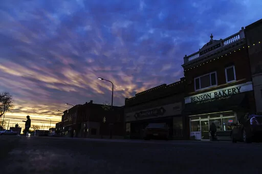 A customer carries a box of baked goods from a bakery at sunrise in Benson, Minn., Wednesday, Dec. 1, 2021. One little town. Three thousand people. Two starkly different realities. It's another measure of how America's divisions don't just play out on cable television. It has seeped into the American fabric, all the way to Benson, where two neighbors, each in his own well-kept, century-old home, can live in different worlds. (AP Photo/David Goldman)