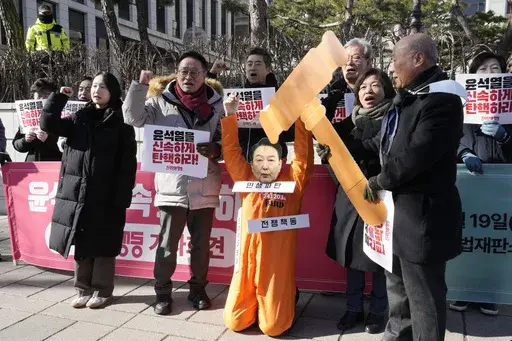 A protester wearing a mask of impeached South Korean President Yoon Suk Yeol attends with his fellow protesters during a rally calling for Yoon to step down in front of the Constitutional Court in Seoul, South Korea, Wednesday, Feb. 19, 2025. The signs read "Impeach Yoon Suk Yeol quickly." (AP Photo/Ahn Young-joon)