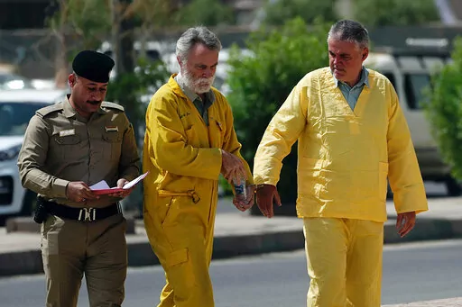 Volker Waldmann, right, and Jim Fitton, center, are handcuffed as they walk to a courtroom in Baghdad, Iraq, Sunday, May 22, 2022. Waldmann and Fitton, accused of smuggling ancient shards out of Iraq, appeared in a Baghdad court Sunday, telling judges they had not acted with criminal intent and had no idea they might have broken local laws. (AP Photo/Hadi Mizban)