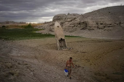 FILE -A man walks by a formerly sunken boat standing upright into the air with its stern buried in the mud along the shoreline of Lake Mead at the Lake Mead National Recreation Area near Boulder City, Nev., June 22, 2022. Divers have found another set of human remains at drought-stricken Lake Mead near Las Vegas. A Lake Mead National Recreation Area statement said Thursday, Oct. 27, 2022 that a National Park Service dive team confirmed on Oct. 18 that a bone believed to be human had been found a