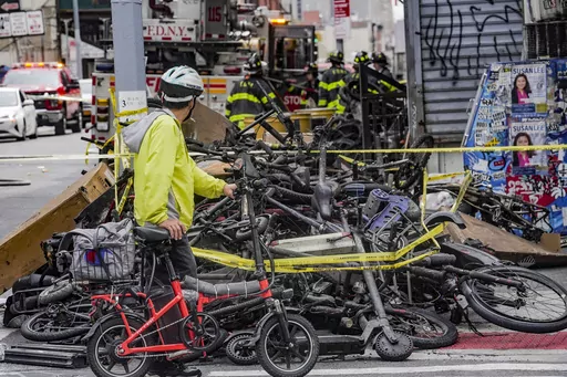 A biker stops to look at a pile of e-bikes in the aftermath of a fire in Chinatown, which authorities say started at an e-bike shop and spread to upper-floor apartments, Tuesday June 20, 2023, in New York. Federal officials are looking into cracking down on defective lithium-ion batteries that power hoverboards, scooters and motorized bicycles because of a rash of deadly fires caused by exploding batteries. The effort comes as New York City implements new laws meant to reduce the number of fires