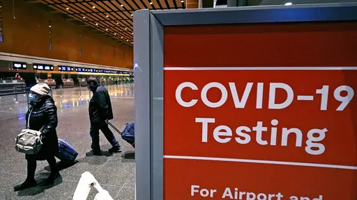 Travelers pass a sign near a COVID-19 testing site in Terminal E at Logan Airport, on Dec. 21, 2021, in Boston. The nation’s top public health agency is expanding a program that tests international travelers for COVID-19 and other infectious diseases. The Centers for Disease Control and Prevention currently operates a program at six U.S. airports that asks passengers from inbound international flights to agree to nose swabs and answer questions about their travel. (AP Photo/Charles Krupa, File