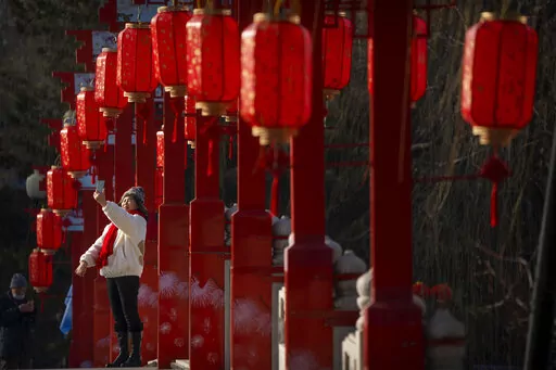 A woman poses for a selfie on a bridge decorated with lanterns at a public park in Beijing on the first day of the Lunar New Year holiday, Sunday, Jan. 22, 2023. (AP Photo/Mark Schiefelbein)