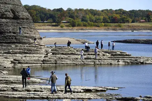 People walk to Tower Rock, an attraction normally surrounded by the Mississippi River and only accessible by boat, Oct. 19, 2022, in Perry County, Mo. Foot traffic to the rock formation has been made possible because of near record low water levels along the river. The impacts of climate change hit communities across the country, yet voters in rural areas are the least likely to feel Washington is in their corner on the issue. (AP Photo/Jeff Roberson, File)