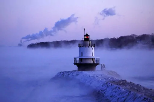 Spring Point Ledge Light is surrounded by arctic sea smoke while emissions from the Wyman Power plant, background, are blown horizontal by the fierce wind, Saturday, Feb. 4, 2023, in South Portland, Maine. The morning temperature was about -10 degrees Fahrenheit. (AP Photo/Robert F. Bukaty)