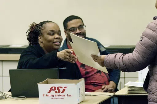 A ballot is handed to a voter, far right, as early voting takes place at the Warren City Hall, Feb. 21, 2024, in Warren, Mich. The Republican National Committee has filed voting-related lawsuits in two dozen states targeting such things as voter rolls, mailed balloting and policies related to poll watchers. Democrats say it’s a strategy designed to raise doubts about the legitimacy of the vote this fall and potentially delay certification of the results. (AP Photo/Carlos Osorio, File)