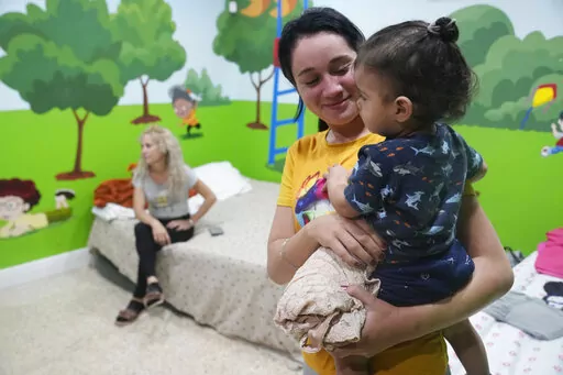 Isabel Bembow Tamayo holds Liam Centeno, 1, in the Iglesia Rescate school classroom that is converted into a bedroom for her family, Tuesday, Feb. 21, 2023, in Hialeah, Fla. Isabel, her mother and two siblings arrived on an overcrowded boat from Cuba. In the last 18 months, an estimated 250,000 migrants and asylum-seekers like her, mostly from Cuba, Nicaragua, Venezuela and Haiti, have made their way to the Miami area, with only precarious legal status and often without work permits. (AP Photo/M