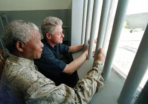 FILE - Nelson Mandela, left, and former US president Bill Clinton look to the outside from Mandela's Robben Island prison cell in Cape Town, South Africa, March 27, 1998. A South African Cabinet minister on Friday Dec. 24, 2021, urged the cancellation of an upcoming U.S. auction of a key to the Robben Island prison cell where Nelson Mandela, the country's first Black president, was long jailed for his opposition to apartheid. (AP Photo/Scott Applewhite, Pool, File)