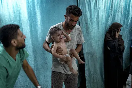 A Palestinian man holds a child wounded in the Israeli bombardment of the Gaza Strip in a hospital in Deir al-Balah, Thursday, July 18, 2024. (AP Photo/Abdel Kareem Hana)