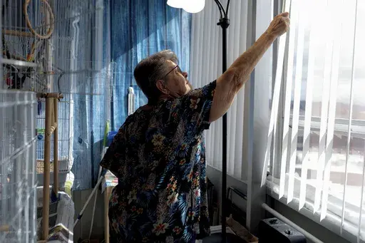 Phyllis Goss opens the window blinds for her birds inside her studio apartment at Smith Tower Apartments on Monday, March 10, 2025, in Vancouver, Wash. (AP Photo/Jenny Kane)