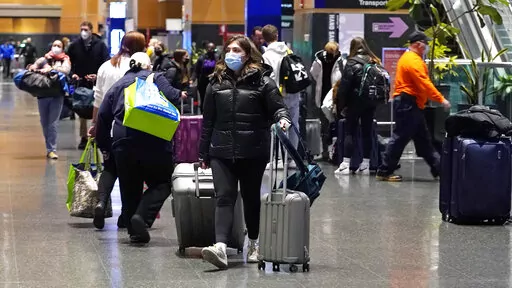 Travelers trek through Terminal E at Logan Airport, Tuesday, Dec. 21, 2021, in Boston.  At least three major airlines say they have canceled dozens of flights, Friday, Dec. 24,  because illnesses largely tied to the omicron variant of COVID-19 have taken a toll on flight crew numbers during the busy holiday travel season.  (AP Photo/Charles Krupa)