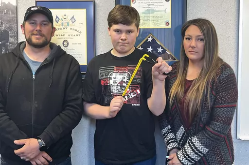 Andrew Burns, left, Owen Burns, center, and Margaret Burns pose with a slingshot Owen used to thwart an alleged kidnapping attempt of his sister, on Wednesday, May 17, 2023, in Alpena Township, Mich. The 13-year-old Michigan boy who used a slingshot to save his 8-year-old sister from an attempted kidnapping on May 10 said he was “freaking out” and simply reached for something that could stop the attack. (Steve Schulwitz/The Alpena News via AP)
