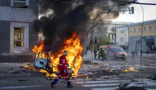 A medical worker runs past a burning car after a Russian attack in Kyiv, Ukraine, Monday, Oct. 10, 2022. The Russian missiles that rained down Monday on cities across Ukraine, bringing fear and destruction to areas that had seen months of relative calm, are an escalation in Moscow's war against its neighbor. But military analysts say it’s far from clear whether the strikes mark a turning point in a war that has killed thousands of Ukrainians and sent millions fleeing from their homes. (AP Phot